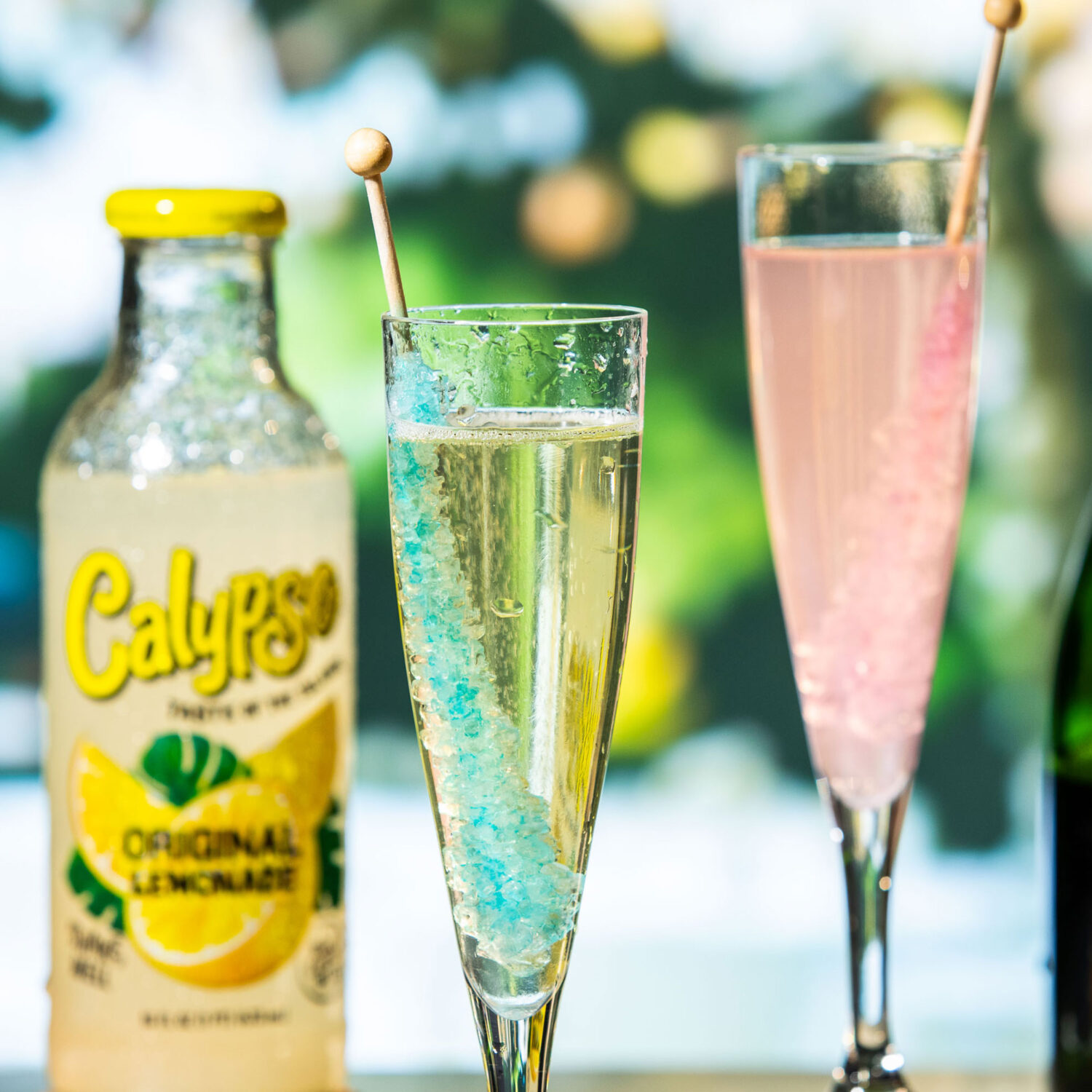 A glass of champagne and rock candy next to a bottle of Calypso Original Lemonade.