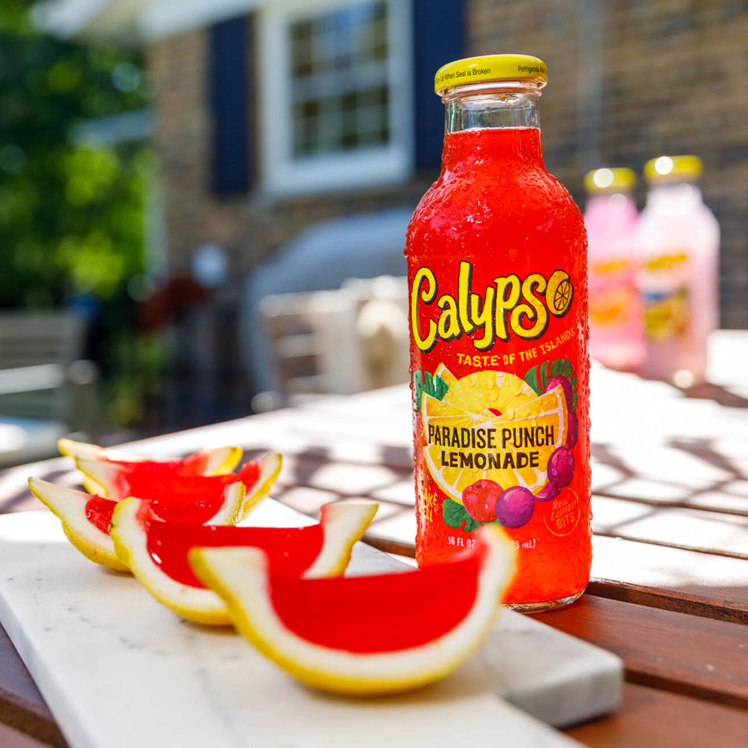 A bottle of Calypso Paradise Punch Lemonade sits on a table next to jello slices in lemon peels.