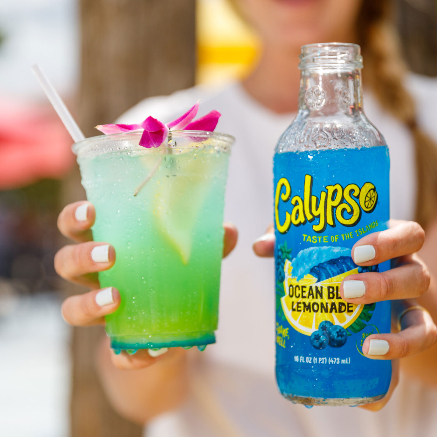 A person holding up a bottle of Calypso Ocean Blue Lemonade and a cocktail.