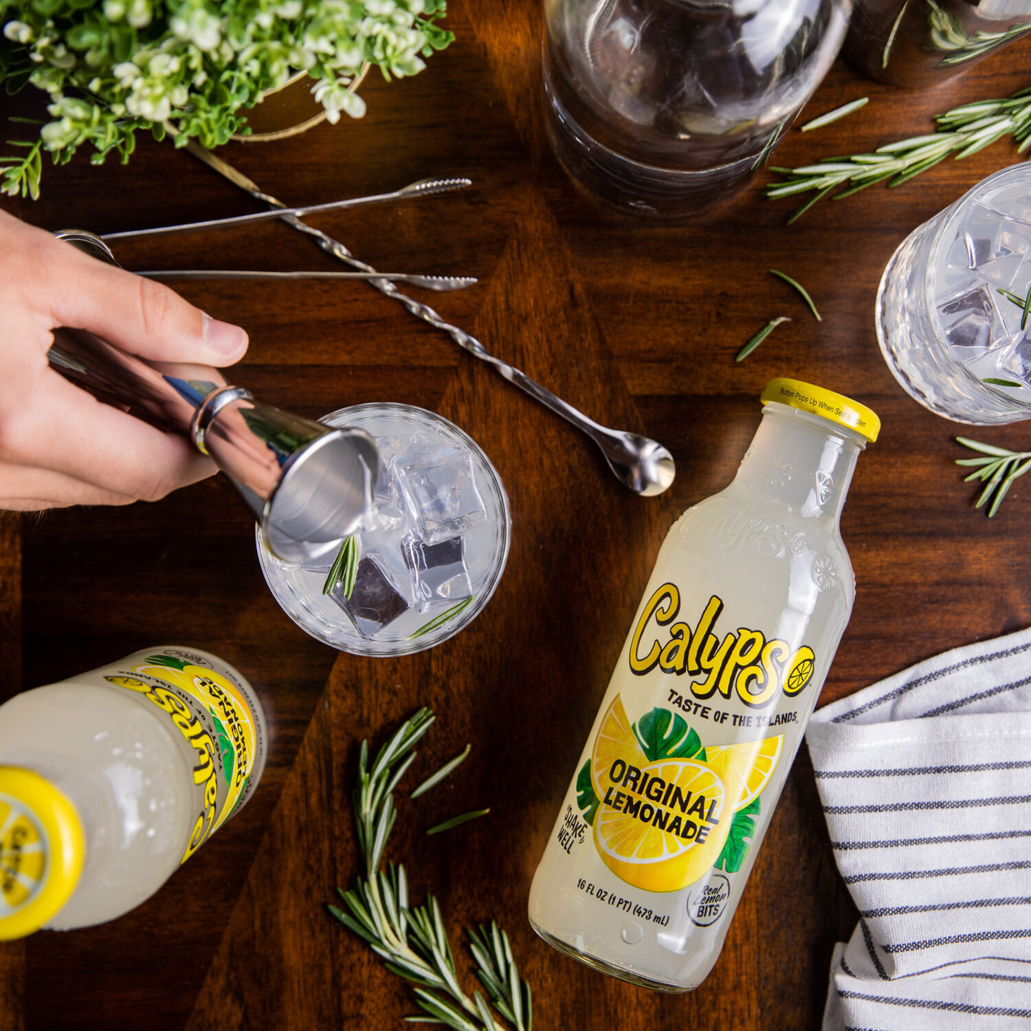 A person is preparing a Calypso Original Lemonade cocktail with rosemary and lemon.
