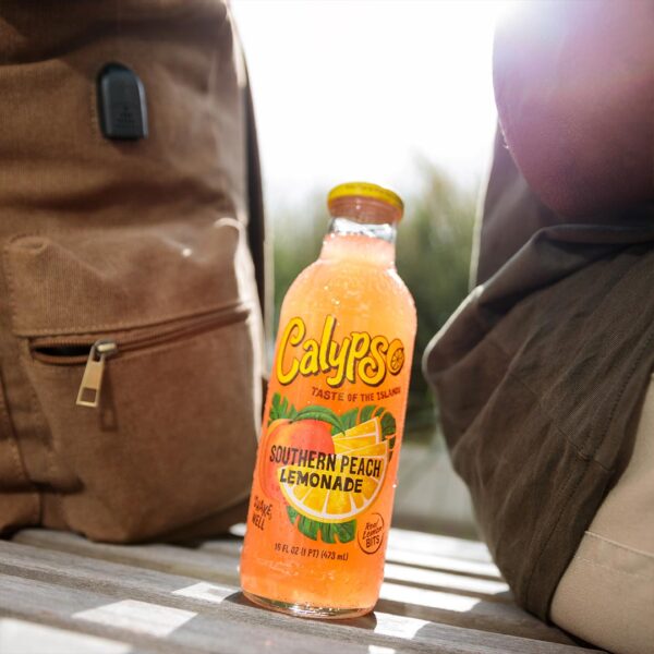 A bottle of Calypso Southern Peach Lemonade sitting on a bench next to a backpack.