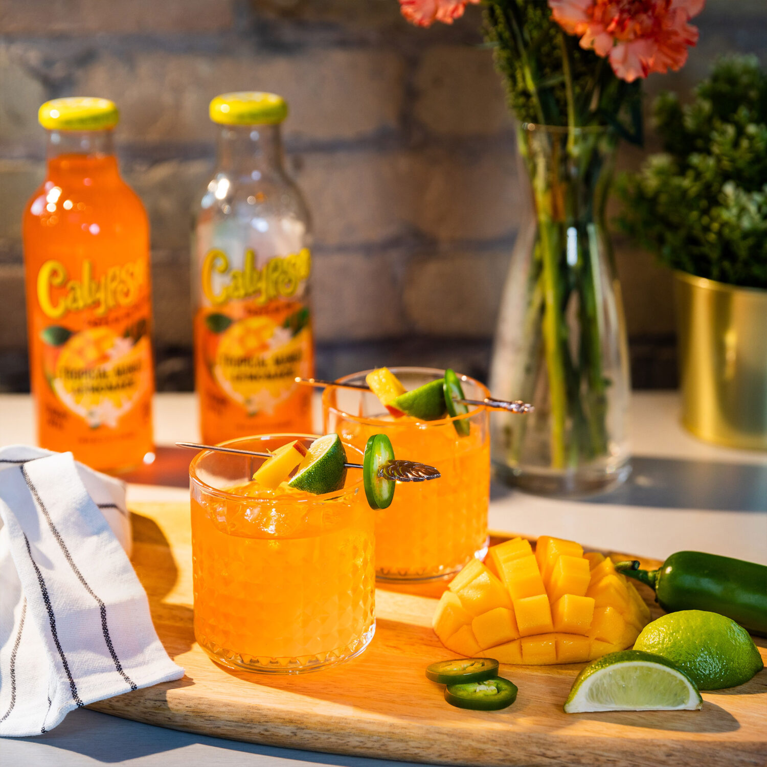 A cocktail of Calypso Tropical Mango Lemonade and cut up mango on a cutting board.