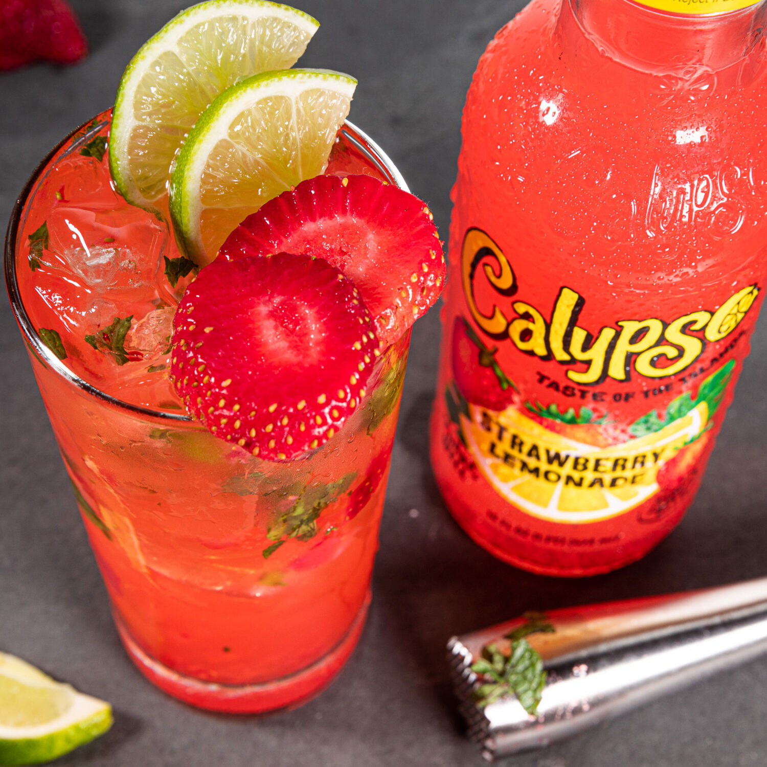 A bottle of Calypso Strawberry Lemonade next to a strawberry and mint cockail.