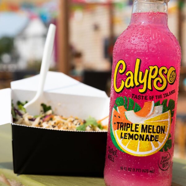 A bottle of Calypso Triple Melon Lemonade on a table next to some take-out food.