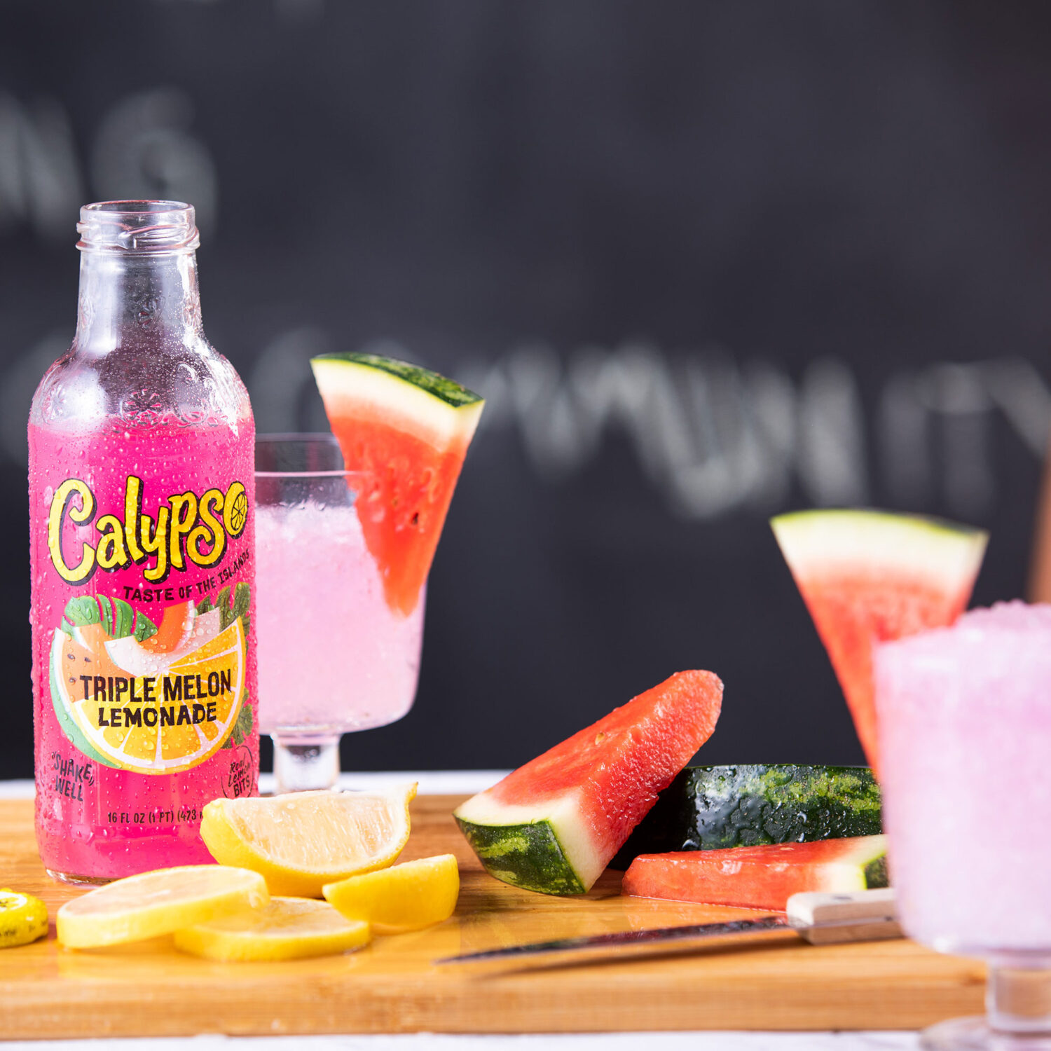 A bottle of Calypso Triple Melon Lemonade on a cutting board with sliced watermelon and lemons.