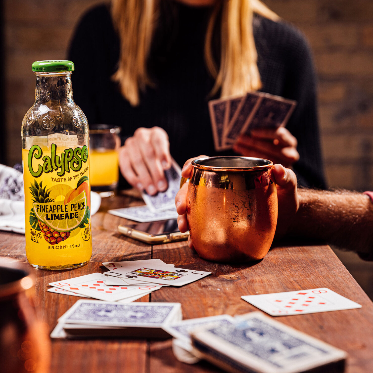 A group of people playing cards at a table while drinking a Calypso Pineapple Peach Limeade cocktail.